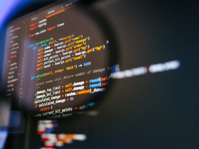 Program code on computer display in magnifying glass. Close-up.